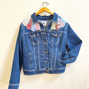 May include: A blue denim jacket with a patchwork collar made of different fabrics in shades of blue, red, and white.