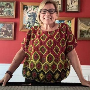 May include: A short-sleeved blouse featuring a repeating pattern of yellow and black teardrop shapes on a deep red background. The garment has a round neckline and a loose, boxy fit, with the fabric displaying visible stitching throughout the surface.