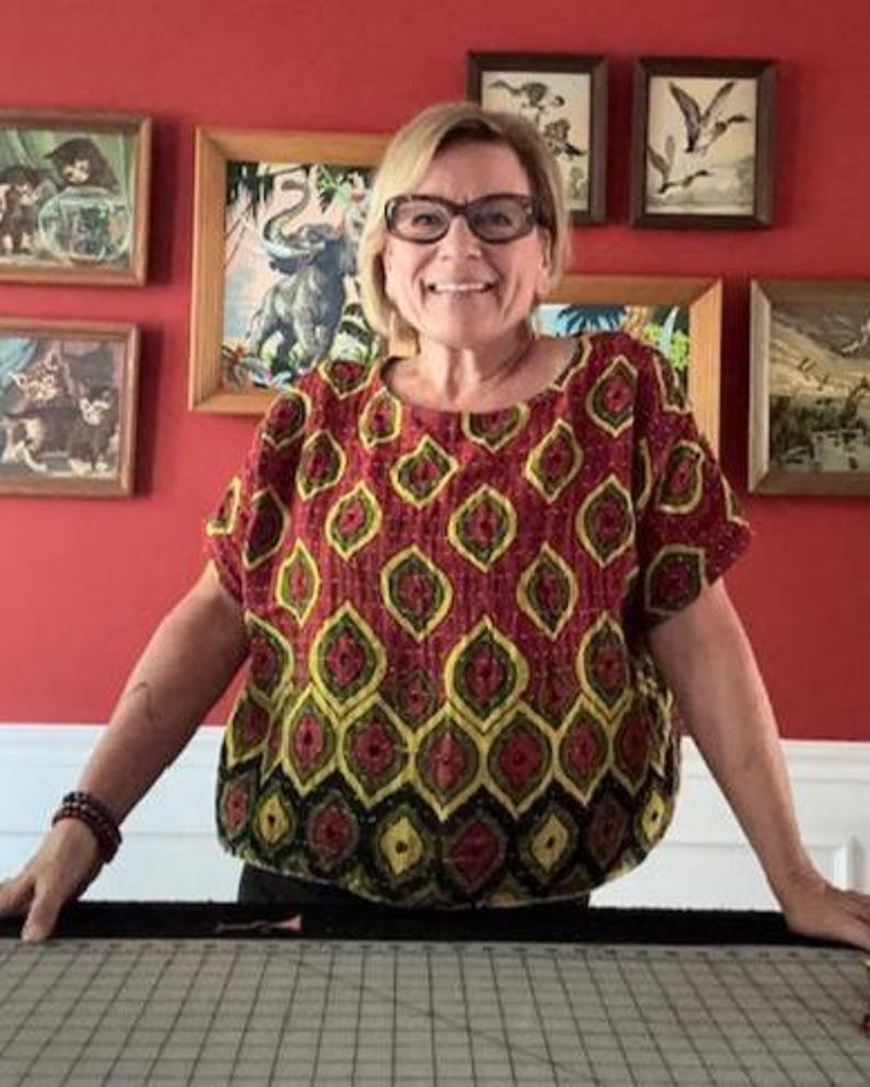 May include: A short-sleeved blouse featuring a repeating pattern of yellow and black teardrop shapes on a deep red background. The garment has a round neckline and a loose, boxy fit, with the fabric displaying visible stitching throughout the surface.
