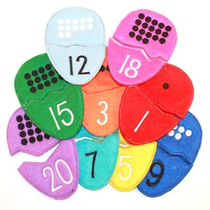 Puede incluir: Un conjunto de diez piezas de rompecabezas de fieltro con forma de huevo, cada una con un color y un número diferente del 1 al 20. Las piezas están diseñadas para que los niños aprendan a contar y a reconocer los números.