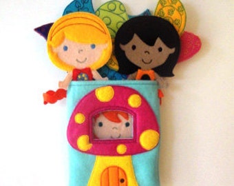 Puede incluir: Una casa de hongo de fieltro con una puerta rosa y una ventana, con tres muñecas de fieltro asomándose. Las muñecas tienen cabello castaño, negro y rubio y visten vestidos coloridos.