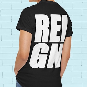 May include: Black t-shirt with the word "REIGN" printed in large, bold, white capital letters. The shirt is short-sleeved and appears to be made of a soft material. The person wearing the shirt is facing away from the camera.