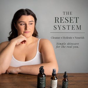 May include: Three amber glass skincare bottles labeled The Reset System, including a pump bottle, a spray bottle, and a dropper bottle. Text on the right reads: THE RESET SYSTEM, Cleanse &bull; Hydrate &bull; Nourish, Simple skincare for the real you.