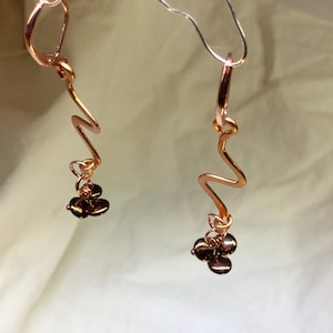 May include: A pair of rose gold earrings with a wavy design and dangling brown beads.
