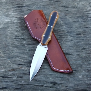 May include: A small, silver knife with a brown and black wooden handle. The knife is in a brown leather sheath with white stitching.