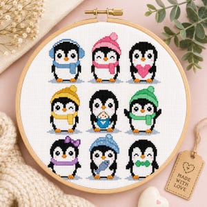 May include: A round wooden embroidery hoop containing a cross-stitch pattern of nine penguins. The penguins are depicted in various winter accessories including colorful hats, scarves, and bows, with some holding items like a heart, a cookie, and a fish.