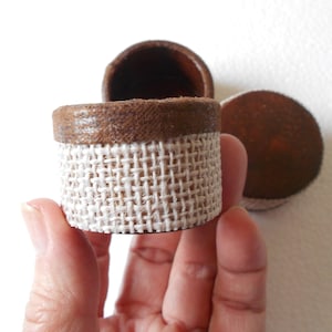 May include: A set of three small, round, brown boxes with a burlap fabric covering the top of one box.