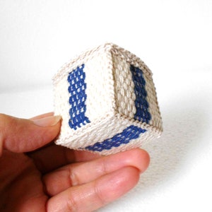 May include: A small, white woven cube with blue stripes. The cube is about the size of a person's hand.