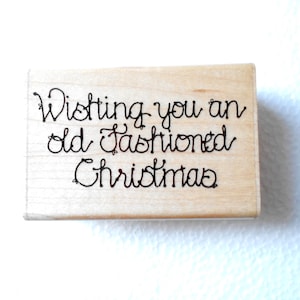 May include: A rectangular wooden stamp with the phrase "Wishing you an old fashioned Christmas" in black cursive lettering. The stamp is light brown and appears to be unused, with a clean surface.