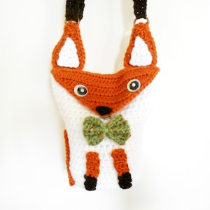 May include: A crocheted fox-shaped bag with a green bow tie. The bag has white fur, orange accents, and black eyes.