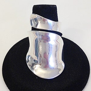 May include: A silver ring with a unique, twisted design. The ring is displayed on a black velvet stand.