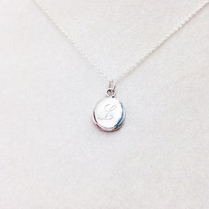 May include: A silver chain necklace with a small oval pendant engraved with the letter "L".