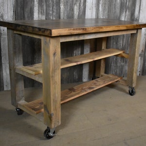 May include: Rustic wooden kitchen island with a distressed brown finish. The island has two shelves and is on wheels.