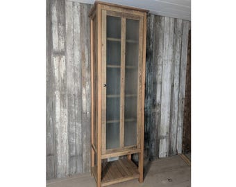 May include: A tall wooden cabinet with glass doors and shelves. The cabinet is made of reclaimed wood and has a rustic finish. It is standing in front of a wall made of wood planks.