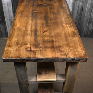 May include: A rustic wooden kitchen island with a distressed brown top and two shelves. The island is on wheels and has a gray-stained base.