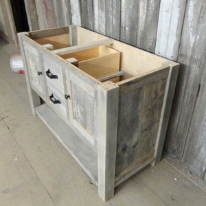 May include: A grey wooden bathroom vanity with two drawers and a lower shelf. The vanity is made from reclaimed wood and has a rustic look.