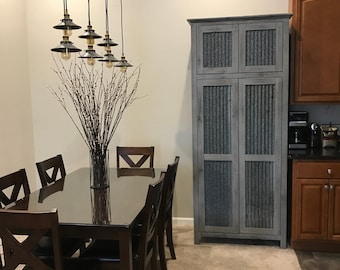 May include: A dining room with a dark wood table and six chairs. The table has a glass top and the chairs have black leather seats. A large cabinet with corrugated metal doors is in the background. The cabinet is painted a light grey colour. There are five black pendant lights hanging from the ceiling.