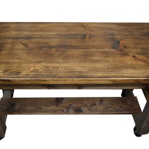 May include: A rustic wooden table with a distressed brown finish. The table has a single shelf and is supported by four legs. The table is on wheels.