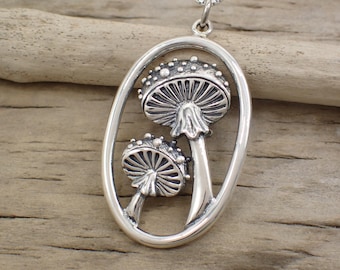 May include: A silver necklace with an oval pendant featuring two detailed mushroom charms. The mushrooms have textured caps and stems.