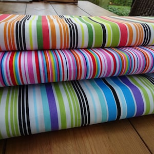 Può includere: Primo piano di tre rotoli di tessuto a righe colorate. Il rotolo superiore presenta strisce rosa, arancioni, verdi e nere. Il rotolo centrale ha strisce rosa, rosse, blu e bianche. Il rotolo inferiore ha strisce blu, verdi e viola.