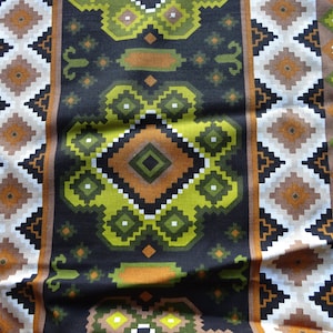 May include: A close-up of a patterned fabric with a repeating geometric design. The pattern features diamonds, squares, and other shapes in shades of brown, white, green, and black. The fabric appears to be a woven material.