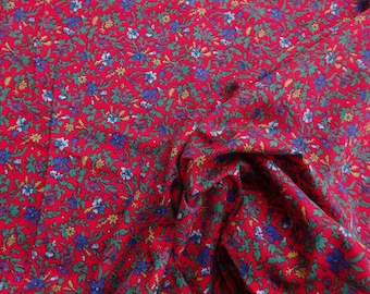 May include: Close-up of red fabric with a floral pattern. The fabric features small blue, purple, and white flowers with green leaves and yellow accents. The fabric is gathered, creating folds and shadows.