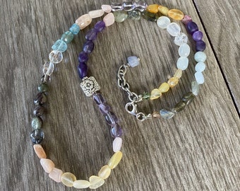 May include: A rainbow gemstone necklace with a silver clasp. The necklace features a variety of stones, including amethyst, aquamarine, citrine, and rose quartz.