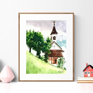 Puede incluir: Pintura acuarela de una iglesia blanca con un techo marr&oacute;n y una cruz en la parte superior. La iglesia est&aacute; rodeada de &aacute;rboles verdes y una colina cubierta de hierba. La pintura est&aacute; enmarcada en un marco de madera.