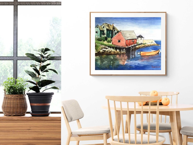 Puede incluir: Pintura acuarela de un paisaje mar&iacute;timo con una casa roja sobre pilotes y un peque&ntilde;o bote naranja en el agua. La pintura est&aacute; enmarcada en un marco de madera claro y est&aacute; colgada en una pared blanca.