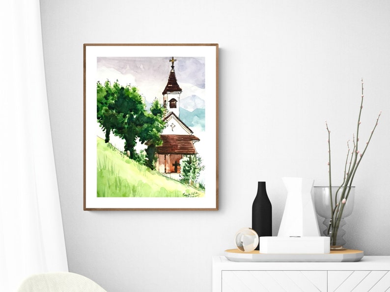 Puede incluir: Pintura acuarela de una peque&ntilde;a iglesia blanca con un techo marr&oacute;n y una cruz en la cima. La iglesia est&aacute; rodeada de &aacute;rboles verdes y una colina cubierta de hierba. El fondo es una acuarela de color p&uacute;rpura y azul, que sugiere una cordillera.
