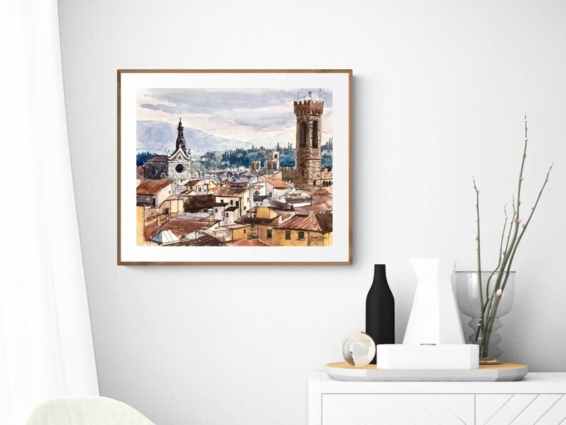 May include: Watercolor painting of a cityscape with a tall tower and a church in the background. The buildings are painted in shades of brown, orange, and yellow. The sky is a light blue with clouds.