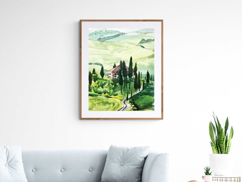 May include: Watercolor painting of a green landscape with a winding road leading to a small house. The painting is framed in a light wood frame.