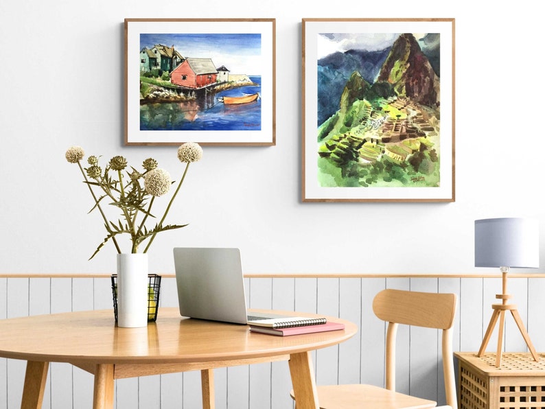Puede incluir: Dos acuarelas enmarcadas en una pared blanca. La pintura de la izquierda muestra una casa roja en una costa con un peque&ntilde;o bote en el agua. La pintura de la derecha muestra una monta&ntilde;a verde con una estructura de piedra en el lado.