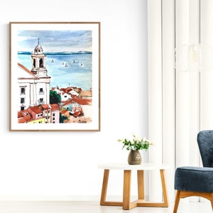 Pu&ograve; includere: Dipinto ad acquerello di un paesaggio urbano con un edificio di chiesa bianco e un'estensione d'acqua blu sullo sfondo. Il dipinto &egrave; incorniciato in una cornice di legno chiaro.