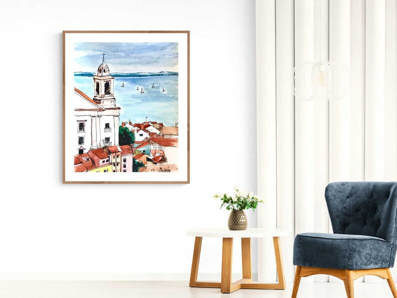 Pu&ograve; includere: Dipinto ad acquerello di un paesaggio urbano con un edificio di chiesa bianco e un'estensione d'acqua blu sullo sfondo. Il dipinto &egrave; incorniciato in una cornice di legno chiaro.