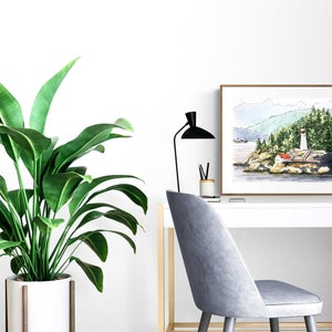 May include: A watercolor painting of a lighthouse on a rocky island with a red roof and white walls. The lighthouse is surrounded by green trees and a body of water. The painting is framed in a brown wood frame and is hanging on a white wall.