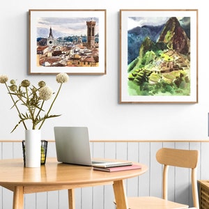 May include: Two framed watercolor paintings, one depicting a cityscape with a tall tower and the other showing a mountain range with a stone structure.