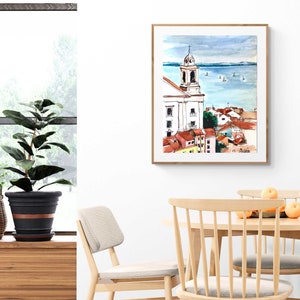 Pu&ograve; includere: Dipinto ad acquerello di una citt&agrave; con un campanile di chiesa e uno specchio d'acqua sullo sfondo. Il dipinto &egrave; incorniciato in una cornice di legno chiaro.