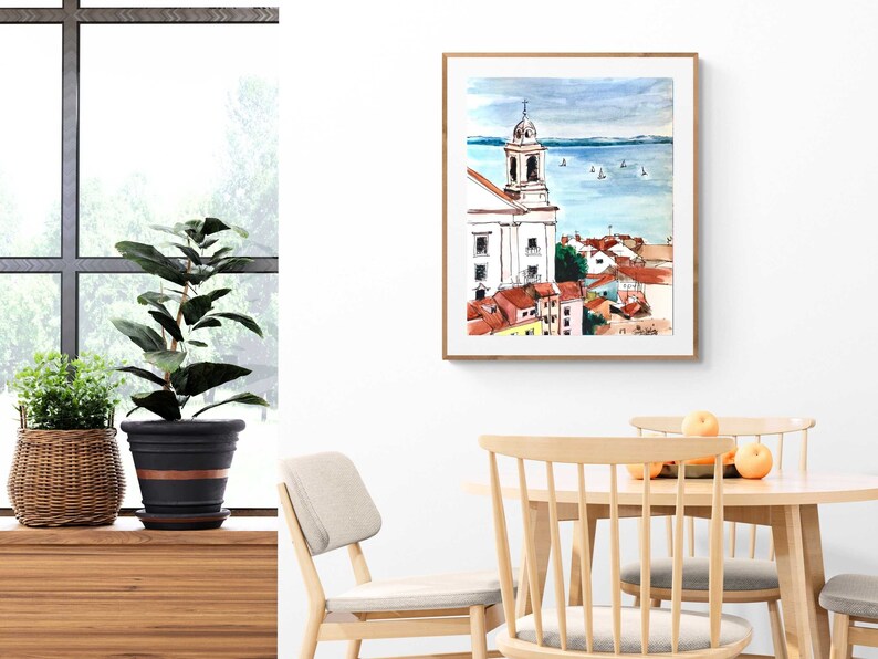 Pu&ograve; includere: Dipinto ad acquerello di una citt&agrave; con un campanile di chiesa e uno specchio d'acqua sullo sfondo. Il dipinto &egrave; incorniciato in una cornice di legno chiaro.