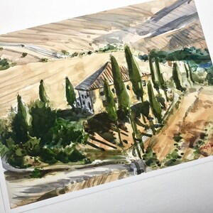 May include: Watercolor painting of a house with a terracotta roof and a row of cypress trees in front of it. The house is set against a backdrop of rolling hills and a blue sky.