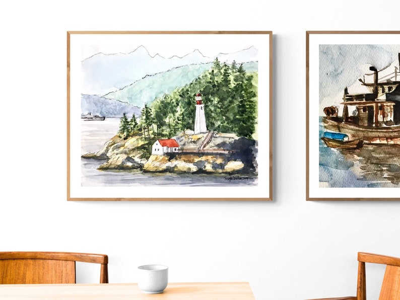 May include: Watercolor painting of a lighthouse on a rocky island with a red roofed house and green trees. The lighthouse is white with a red top and is surrounded by water. The painting is framed in a light wood frame.