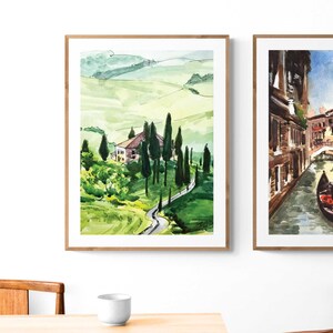 May include: Two watercolor paintings in wooden frames. The painting on the left depicts a green rolling hillside with a small house and trees. The painting on the right shows a canal in Venice with a gondola and a gondolier.