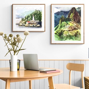 May include: Two framed watercolor paintings on a white wall. The painting on the left depicts a lighthouse on a rocky island with a forest in the background. The painting on the right depicts a mountain range with a stone structure built into the side of the mountain.