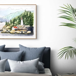 May include: Watercolor painting of a lighthouse on a rocky island with a red roofed building and green trees in the background. The painting is framed in a light wood frame.