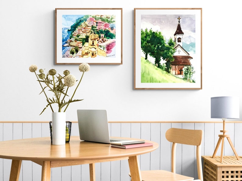Puede incluir: Dos acuarelas enmarcadas. La primera pintura representa un pueblo italiano colorido en un acantilado con vistas al mar. La segunda pintura muestra una iglesia blanca con un techo marr&oacute;n en una colina verde.
