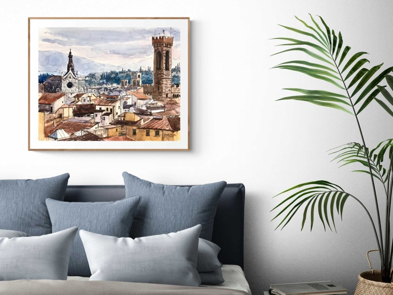 May include: A watercolor painting of a cityscape with a tall tower and a church in the background. The buildings are painted in shades of brown, orange, and yellow, and the sky is a light blue with gray clouds.