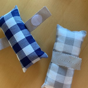 May include: Two fabric pillows with a gingham pattern. One pillow is blue and white, the other is gray and white. Both pillows have a gray fabric strap.
