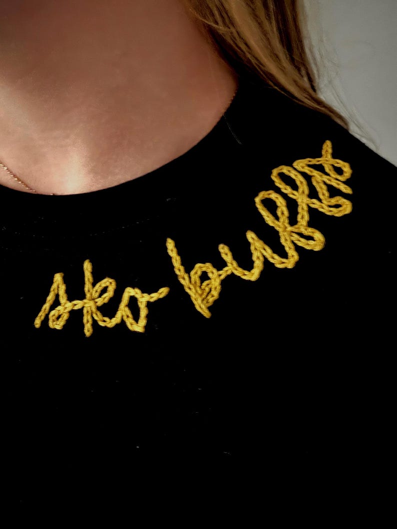 May include: Black crew neck shirt with the embroidered text "Ako bulls" in yellow thread. The shirt is made of a soft material and is suitable for casual wear.