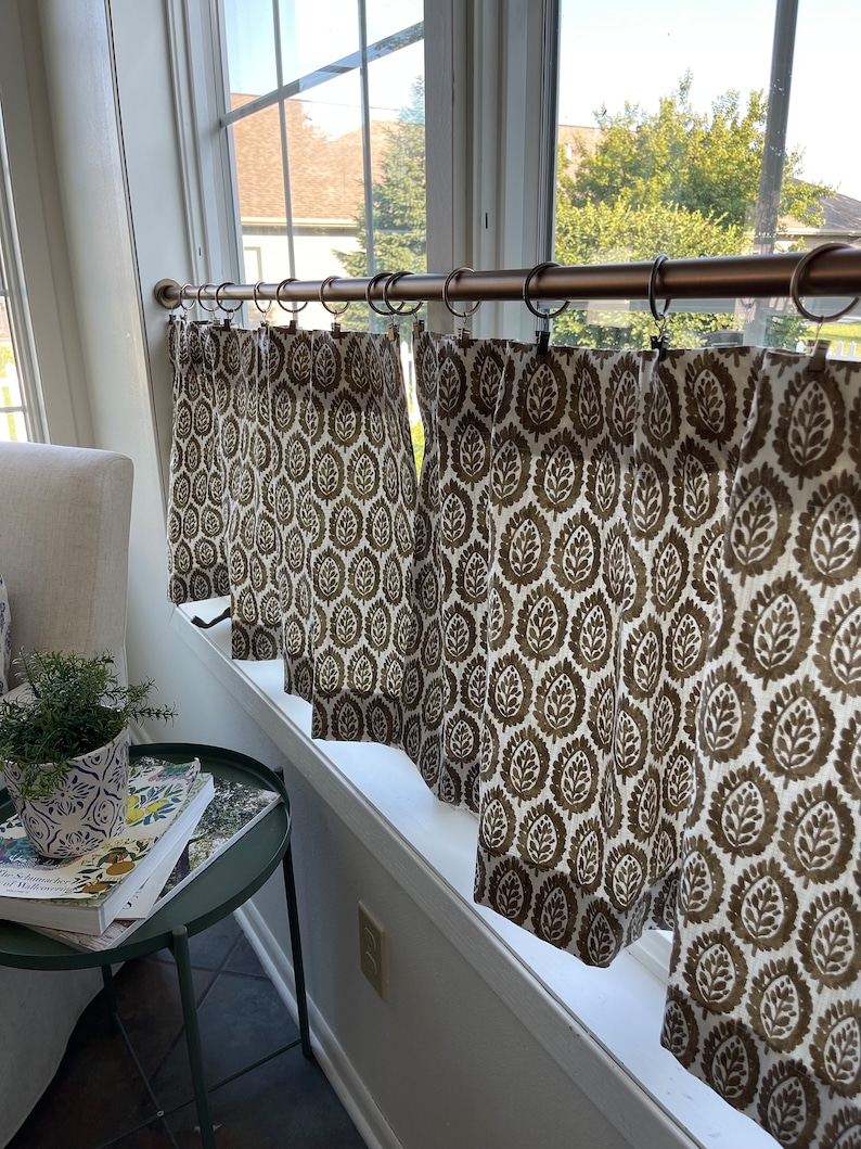 May include: A set of brown and white patterned cafe curtains with a copper curtain rod. The curtains are hung on a window with a white trim.