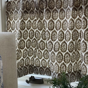 May include: A pair of brown and white patterned valance curtains with a brown leaf design. The curtains are hung on a brass curtain rod with rings.